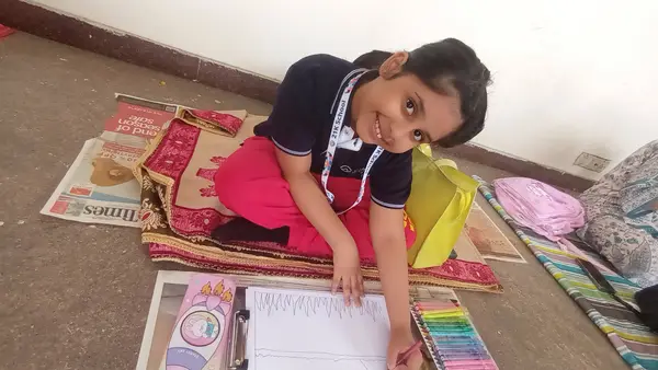 A young learner smiling up from her drawing