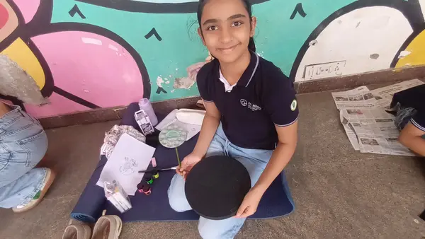 A learner smiling beside the mural with her artwork