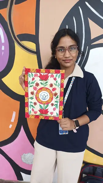 A learner holding her floral folk-art painting in front of the mural