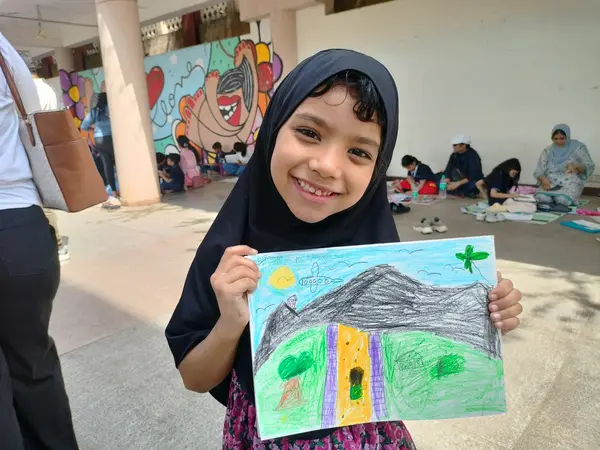 A learner in a hijab smiling with her landscape drawing