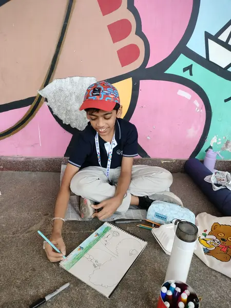 A learner in a red cap sketching beside the mural