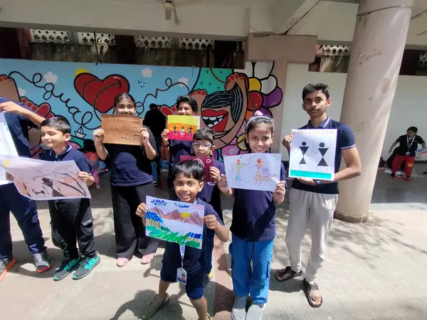 Learners hold up their artworks in front of the mural