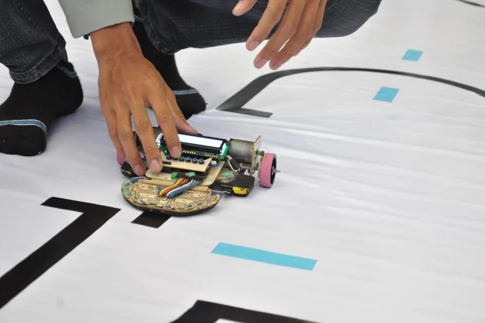 A hand sets a small home-built robot down on a black line-following track taped to the floor