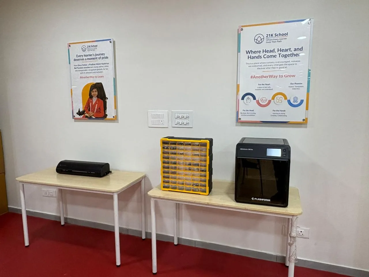 A 3D printer, a parts organiser and a laminator set out on tables under 21K posters
