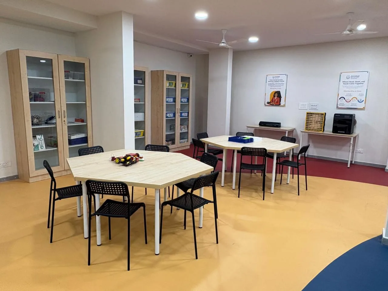 Glass-fronted cabinets of kits beside work tables, with a 3D printer at the back wall