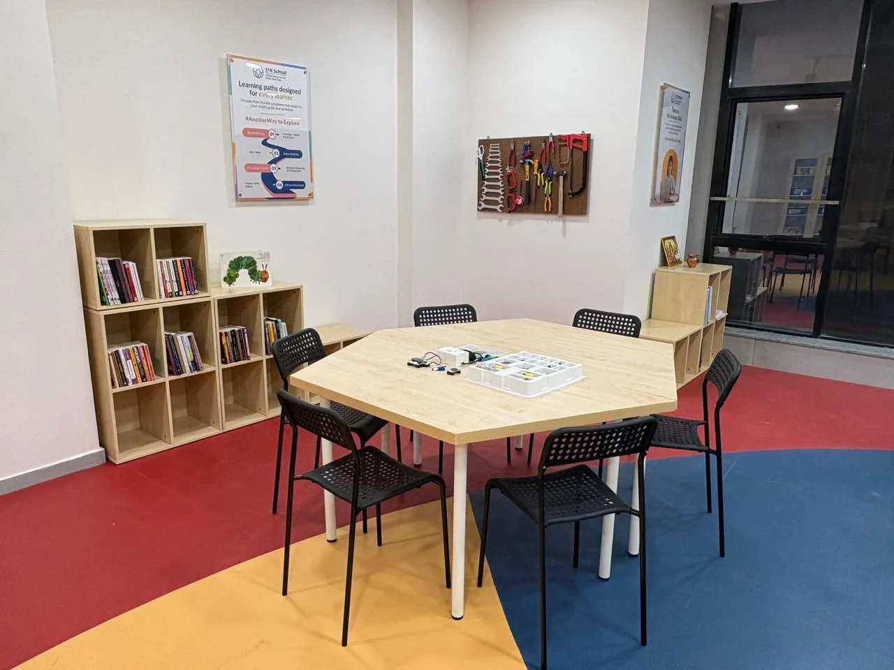 A tray of building kits on a table beside bookshelves and a board of hand tools