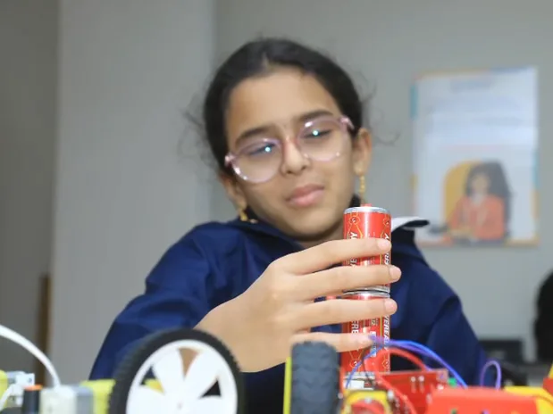 A learner in glasses holds up the battery for her robot car