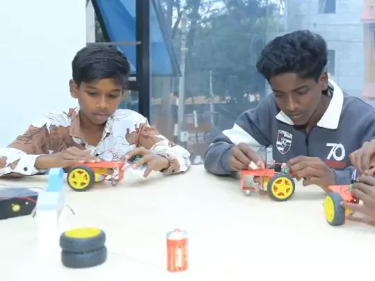 Two learners build small robot cars at a table by the window