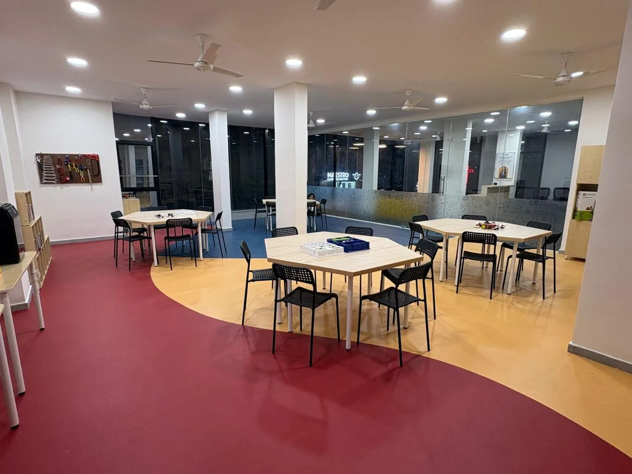 The Learning Garage’s open floor: hexagonal work tables and black chairs on a red, yellow and blue floor