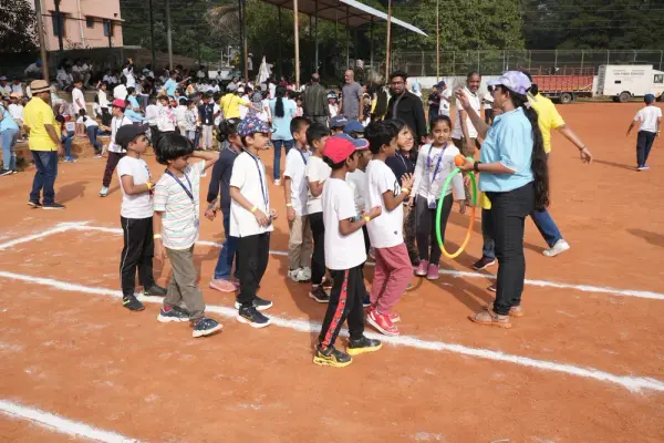 Learners holding hula hoops gather around a facilitator on the red running track at Sports Day in Bengaluru