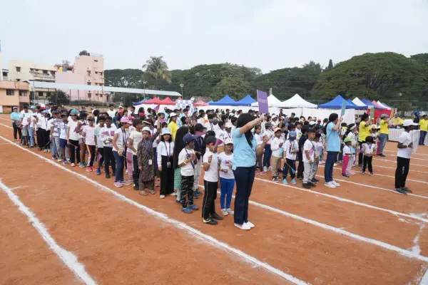 A long line of learners in white T-shirts waits on the track, with event tents behind them