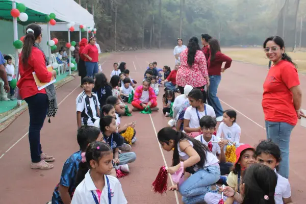 Learners holding pom-poms sit on the track while facilitators in red look on