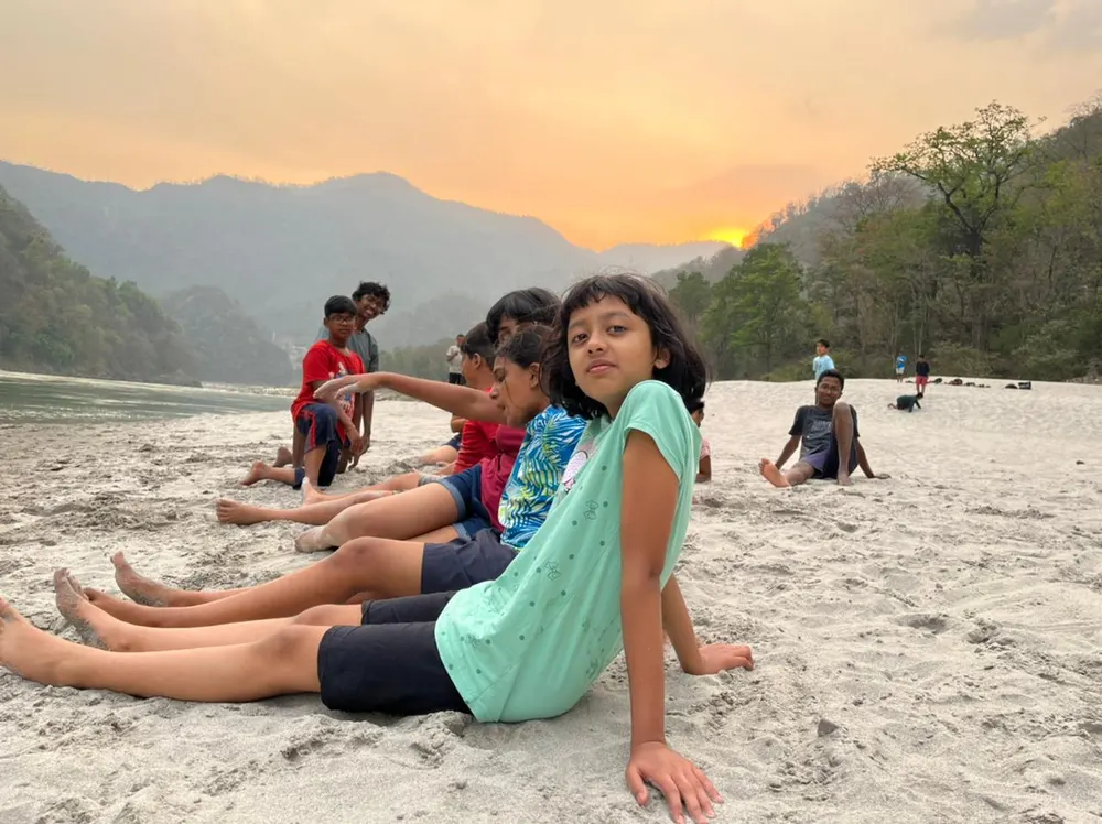 Learners resting on a river beach at sunset in Rishikesh