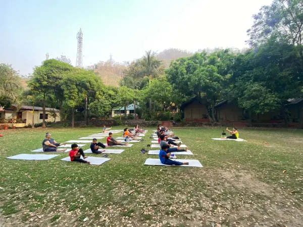 Learners doing yoga on mats on a lawn surrounded by trees