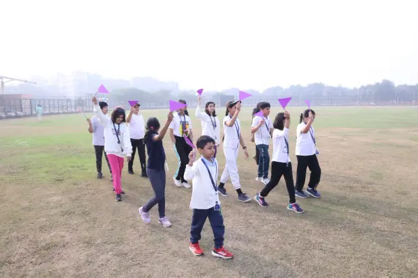 Learners marching across a playing field waving purple flags