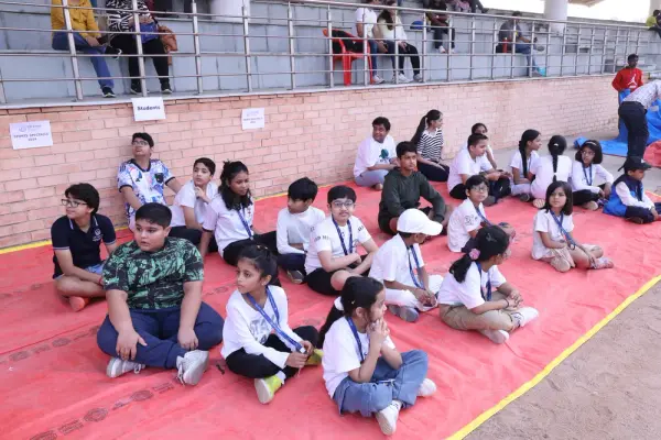 A group of learners sitting cross-legged on a red mat at the stadium