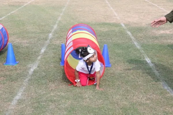 A young learner crawling through a colourful play tunnel on the grass