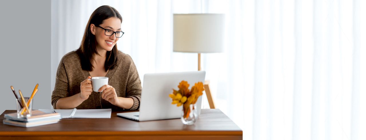 A smiling woman at her desk with a laptop and a cup of tea