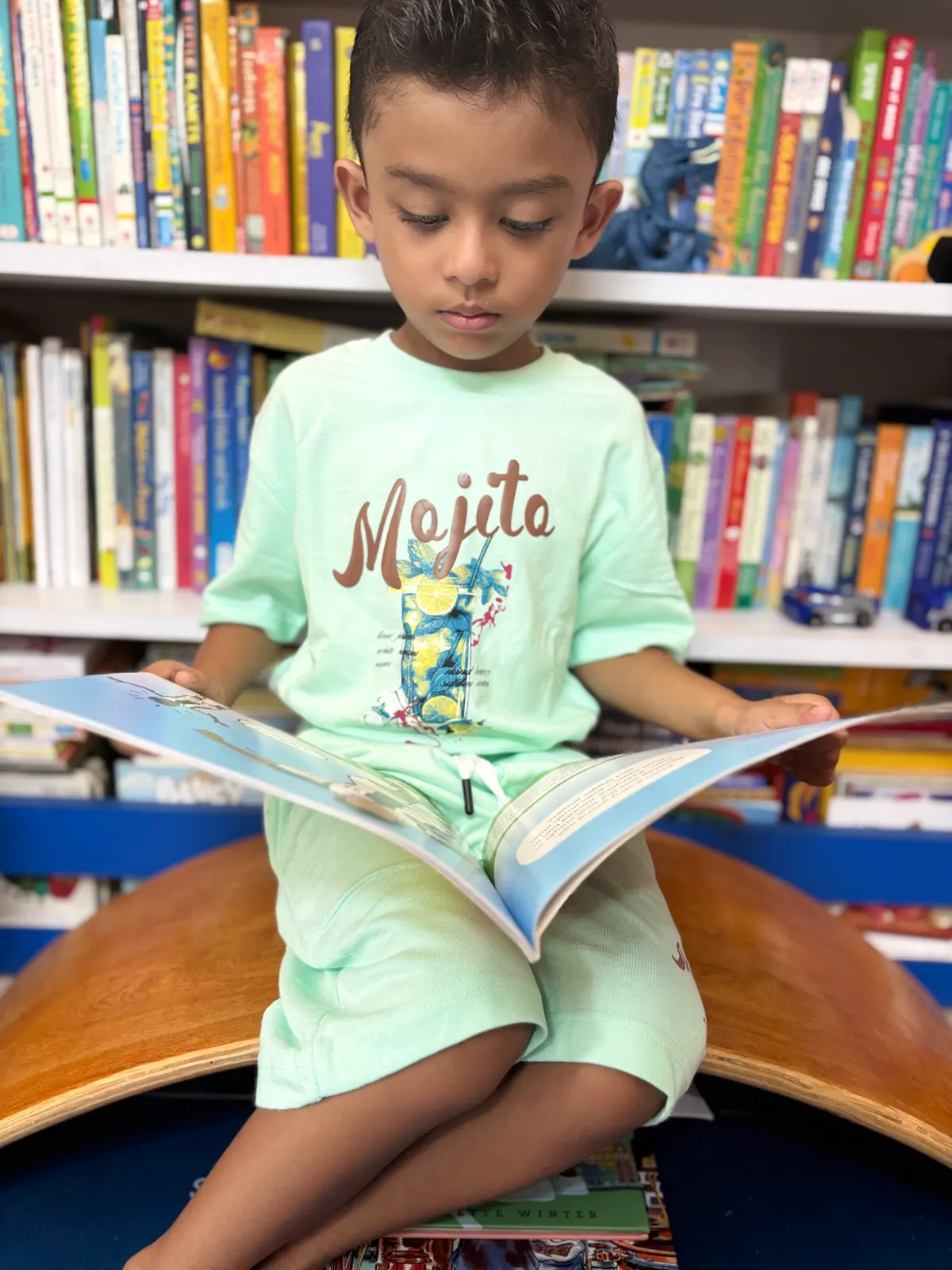 A young learner reading a large picture book in front of full bookshelves