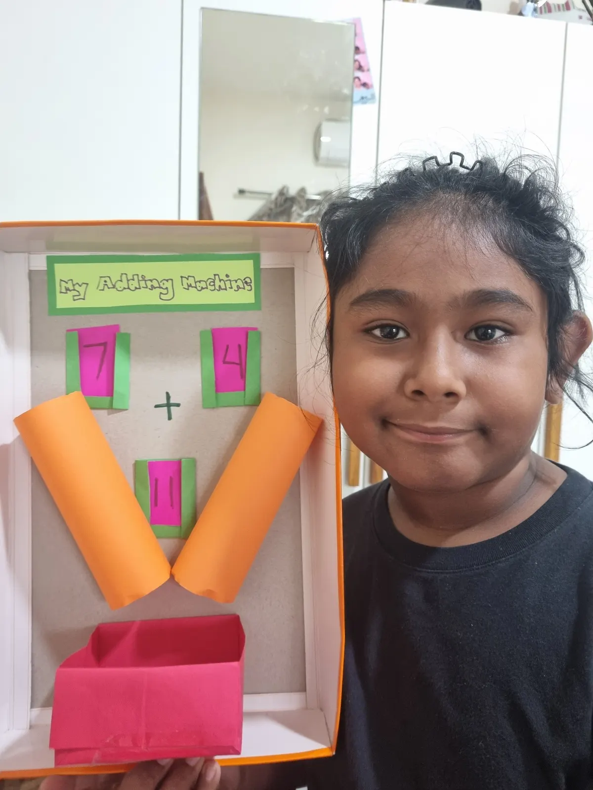 A learner holding up the paper adding machine she made, showing 7 + 4 = 11