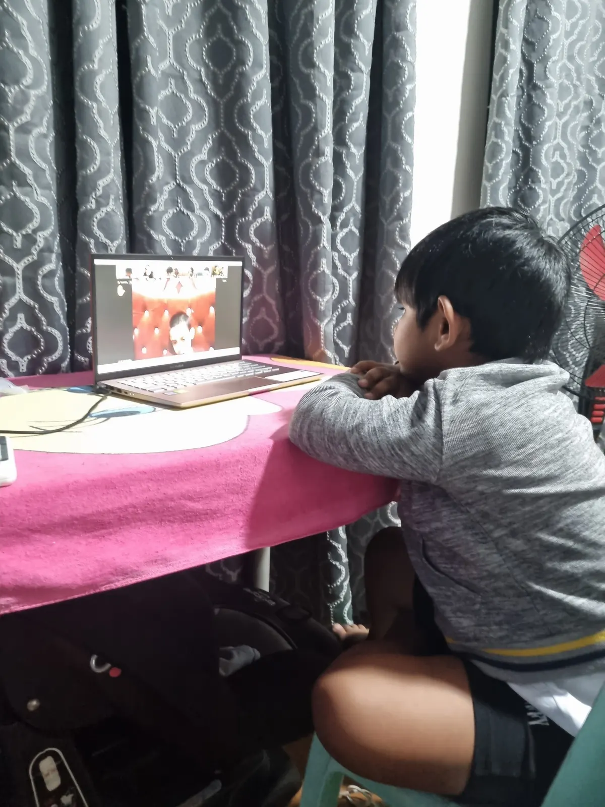 A learner at a table by the window, following a live online class on a laptop