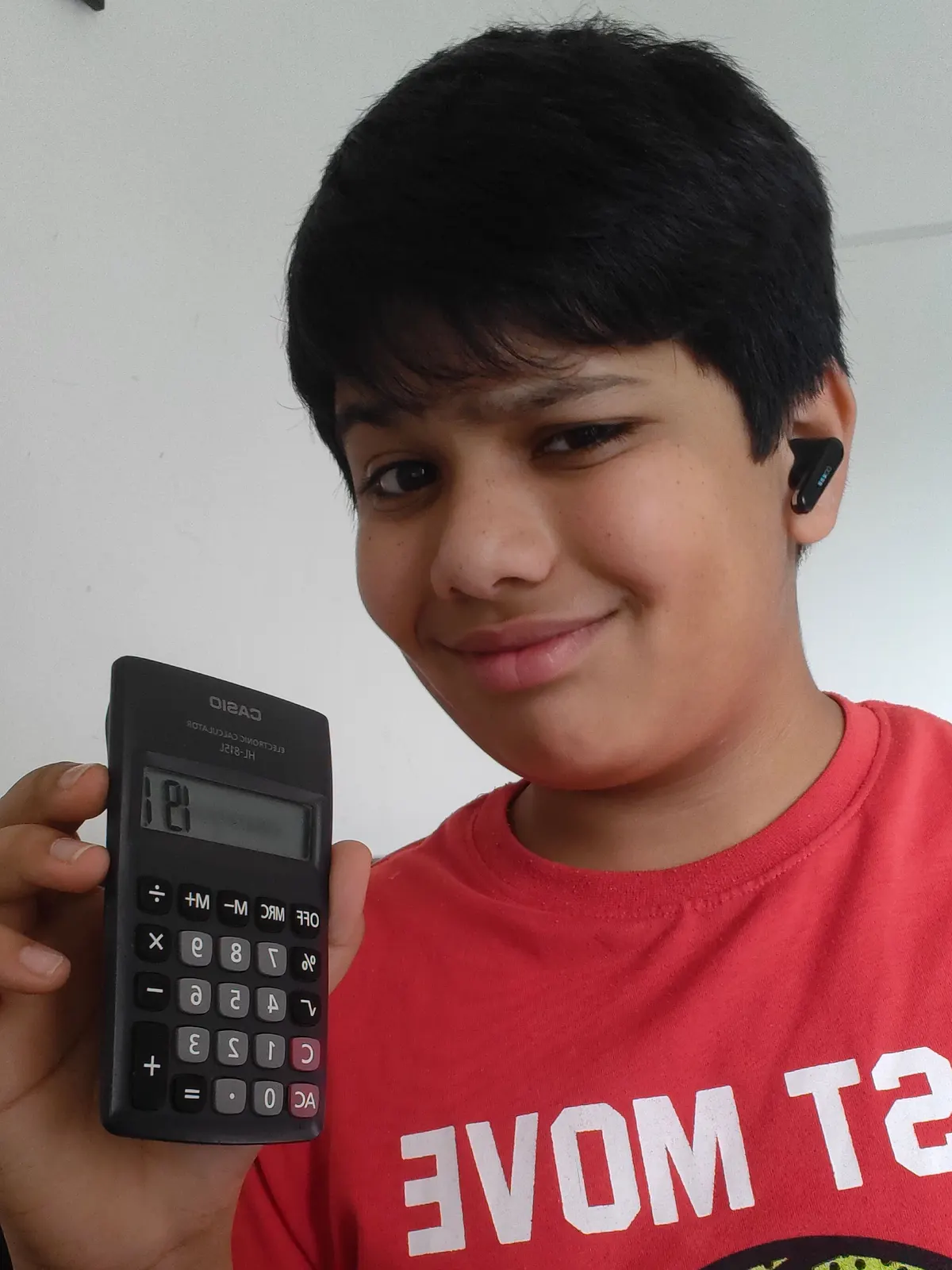 A learner holding up a calculator at his desk