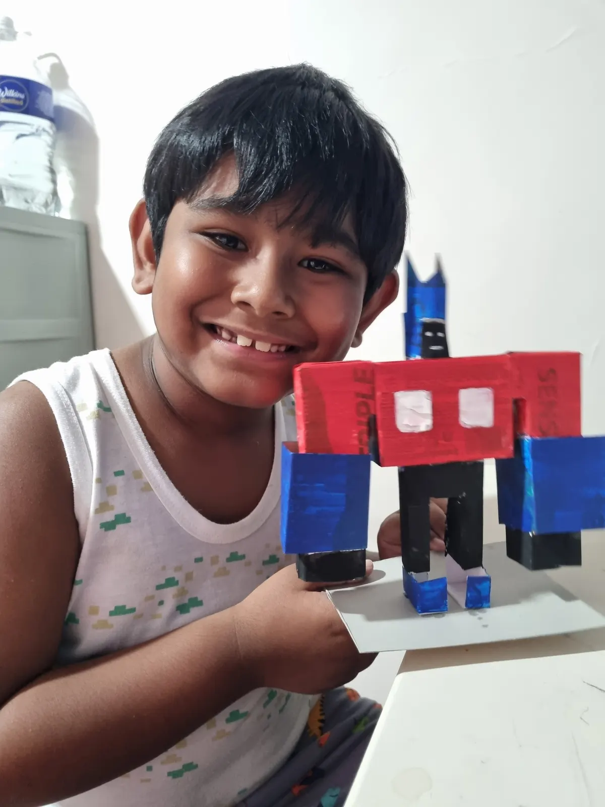 A smiling learner holding the cardboard robot he built and painted