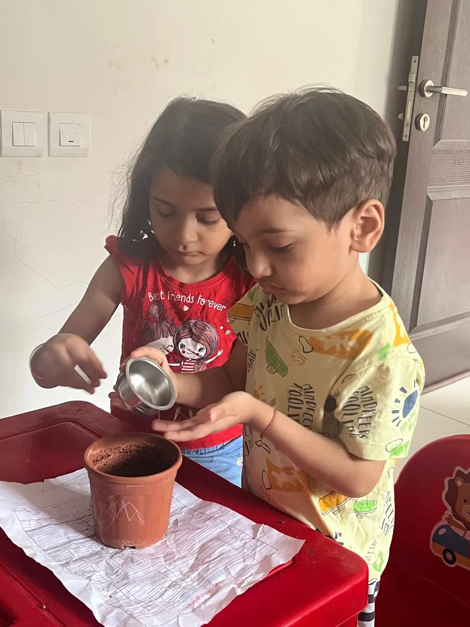 Two young children filling a clay pot with soil at home