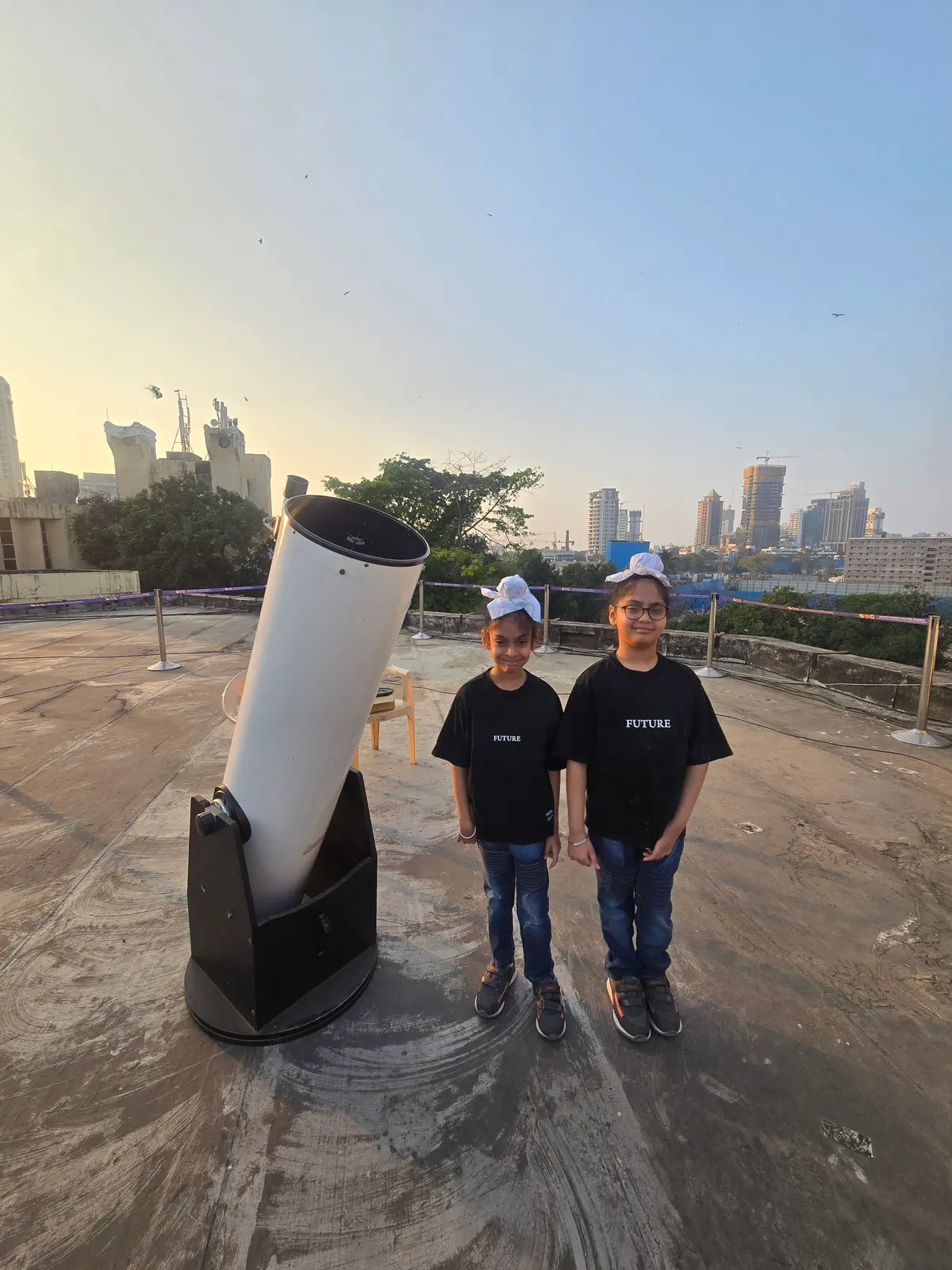 Two learners beside a large telescope on a rooftop at dusk