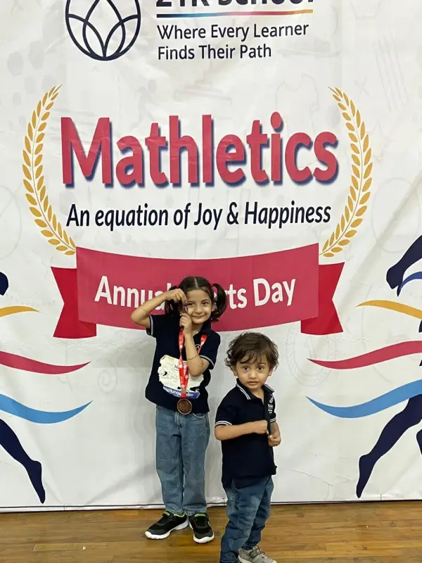 Two young learners in front of the 21K School Mathletics Annual Sports Day backdrop