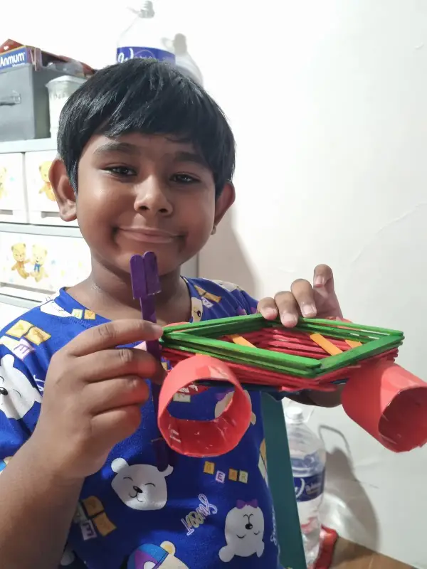 A learner holding up a colourful craft made from ice-cream sticks and paper