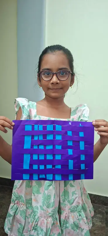 A learner holding a woven paper mat in purple and blue