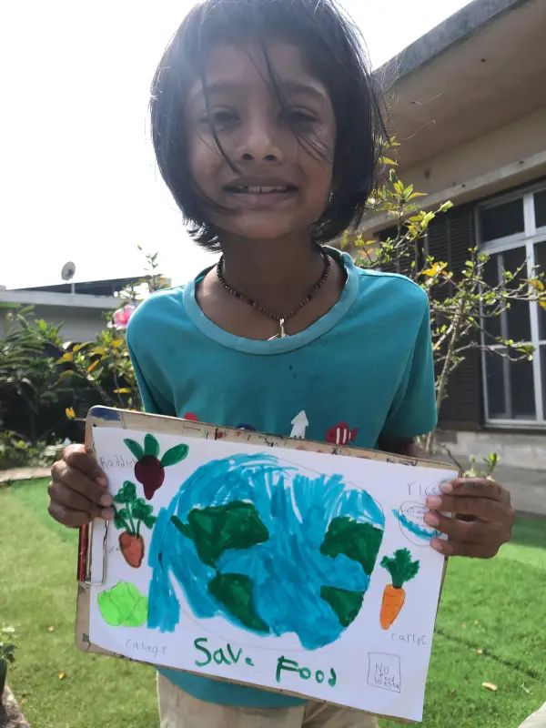 A learner in a garden holding her Save Food poster with a painted Earth