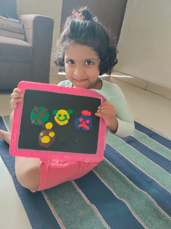 A young learner showing her drawing board of colourful faces