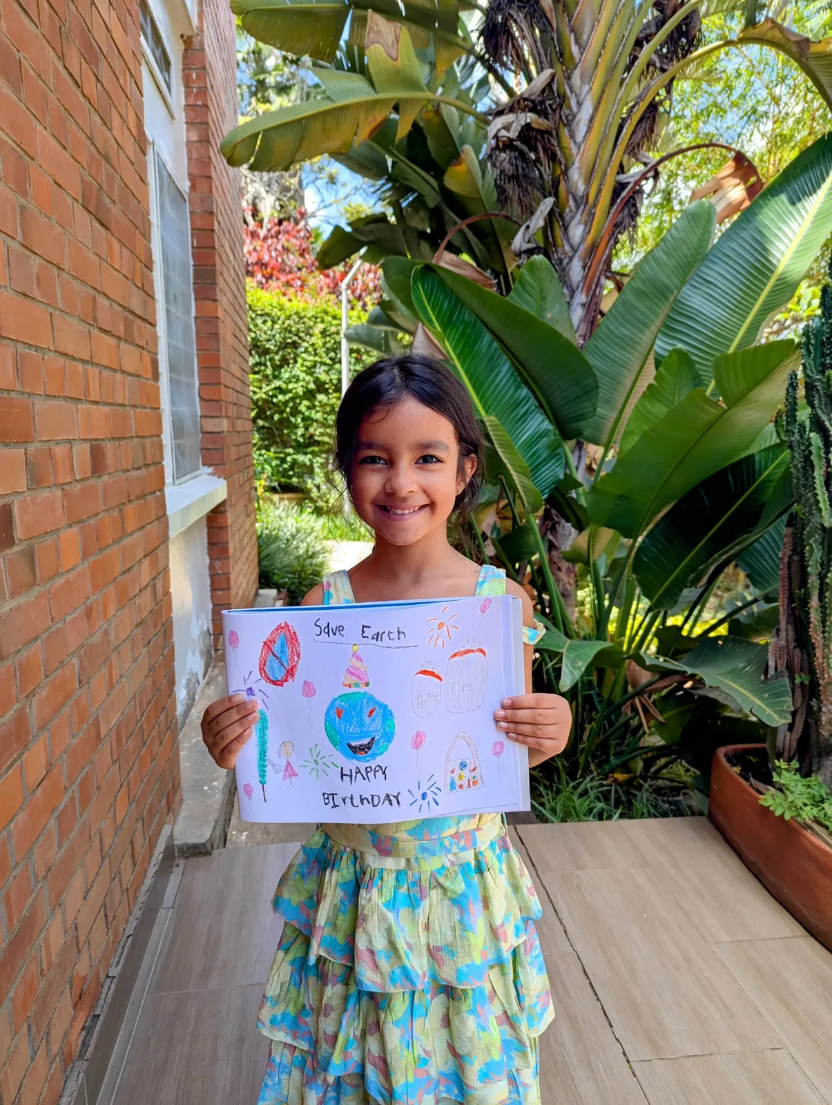 A learner in a garden holding up the poster she drew