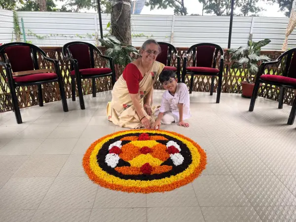 A learner and a grandparent sitting beside a flower rangoli at home