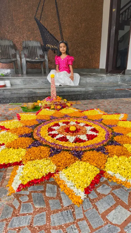 A learner in festive clothes beside a large flower rangoli