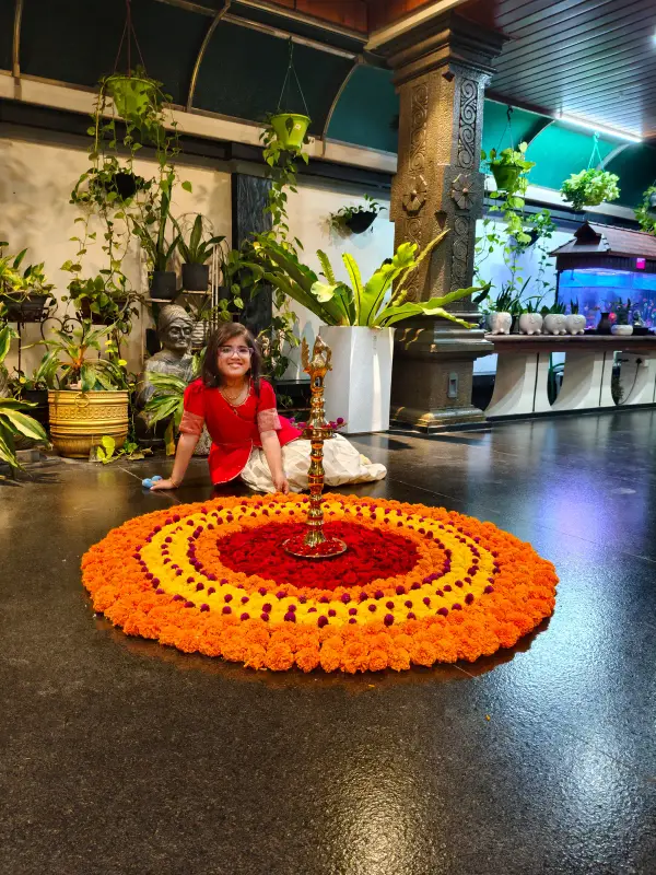 A learner sitting beside a flower rangoli and a brass lamp