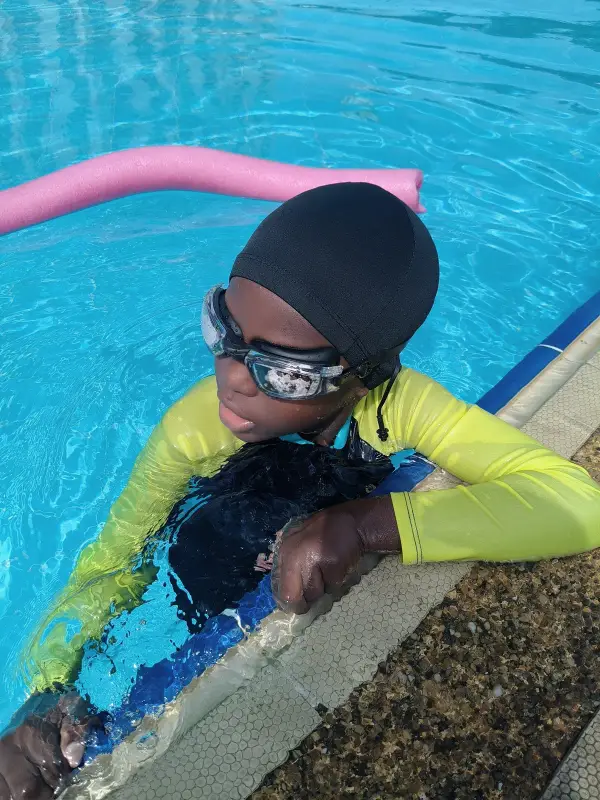 A learner in goggles resting at the pool edge