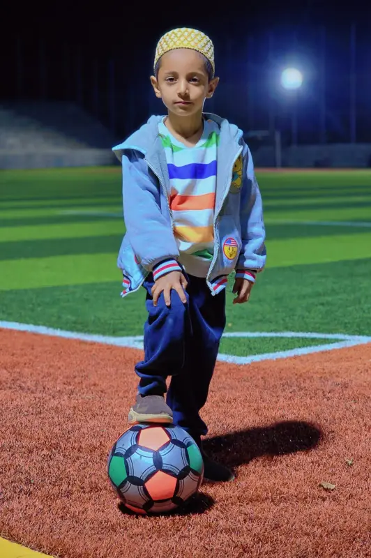 A learner with a football on a floodlit pitch