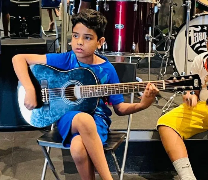 A learner playing an acoustic guitar at a music session