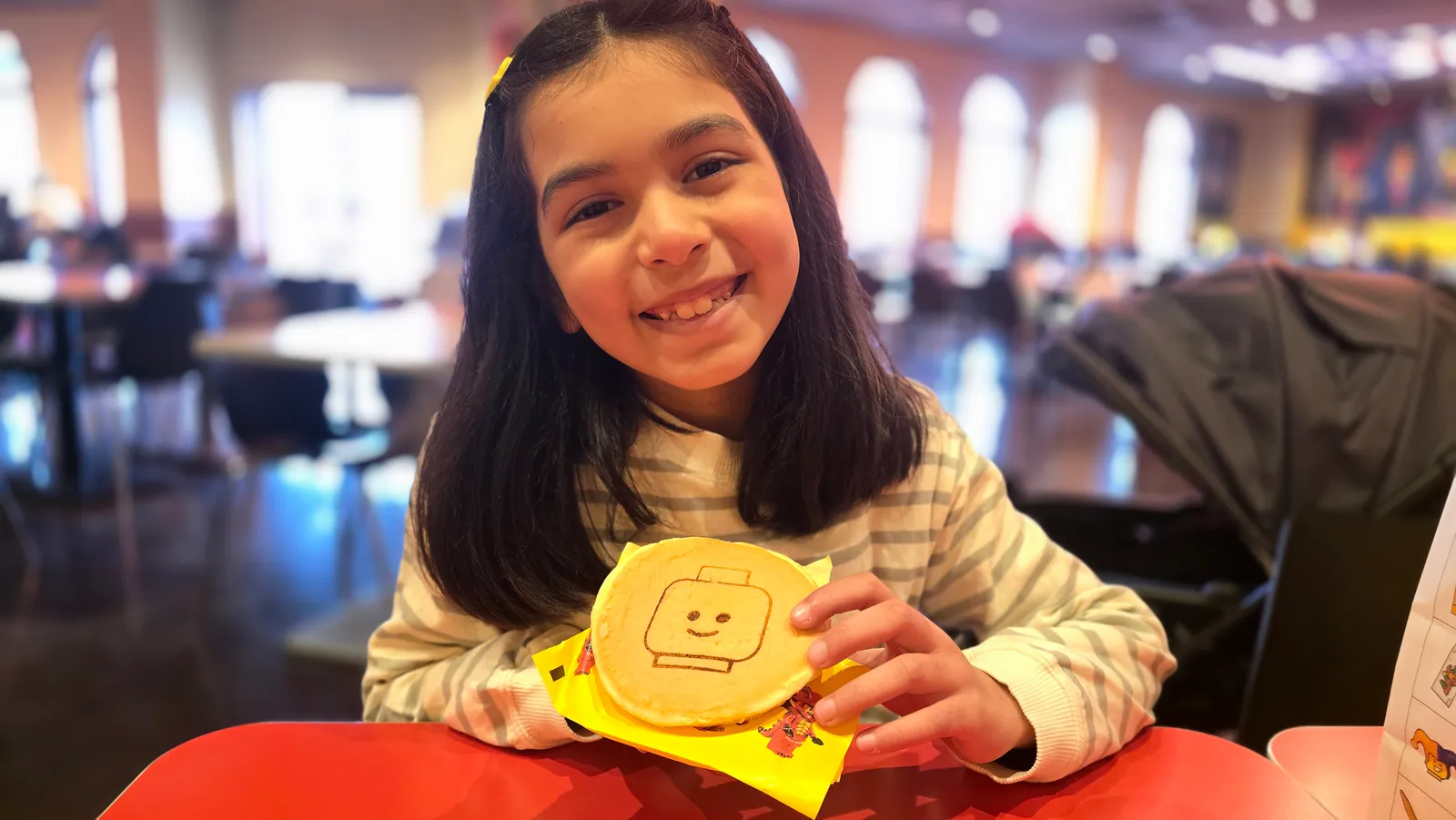 A smiling young learner holding up a cookie at a café table