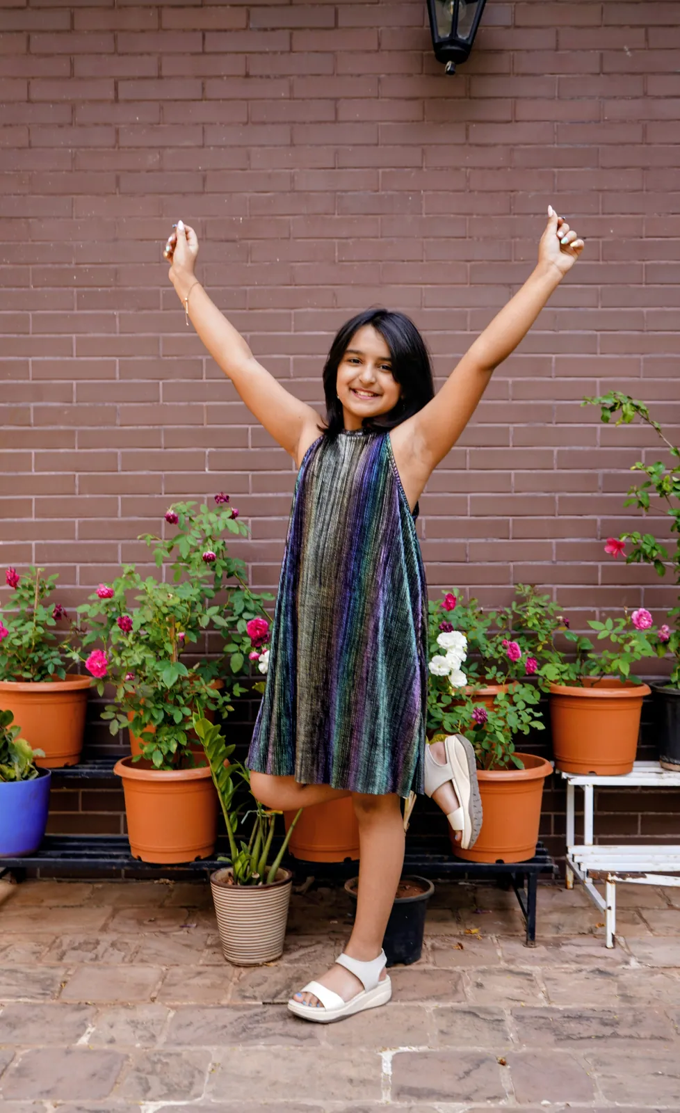 A learner cheering with both arms raised in front of a brick wall and potted plants