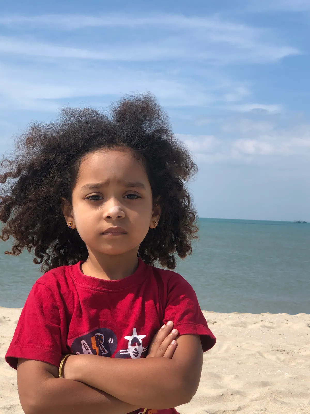 A young learner with curly hair standing confidently on a beach
