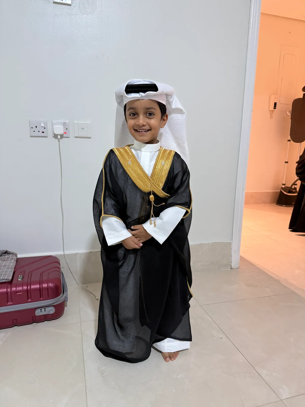 A young learner in traditional Gulf dress, smiling at home
