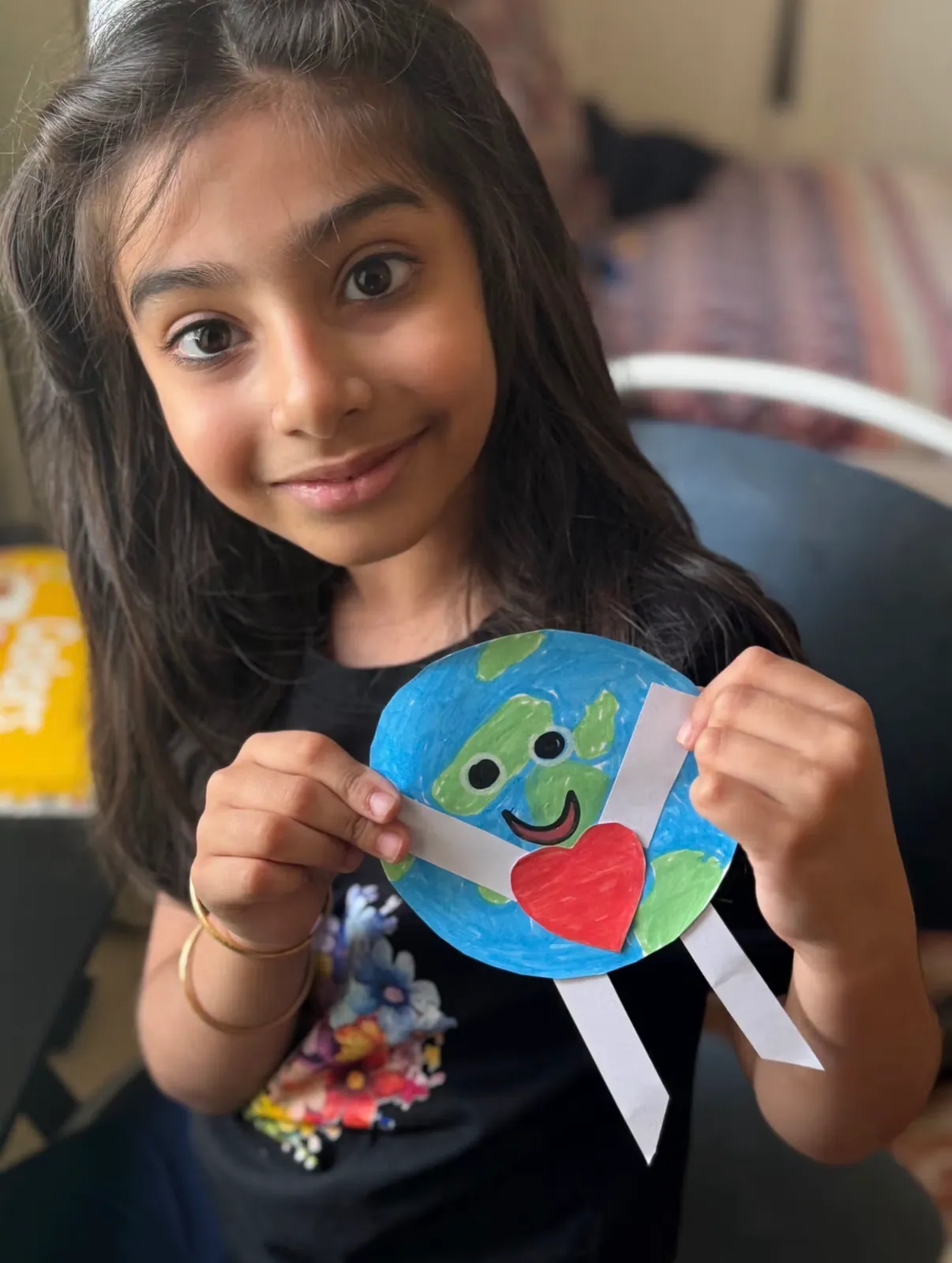 A learner holding up the paper Earth she made, with a heart for the planet