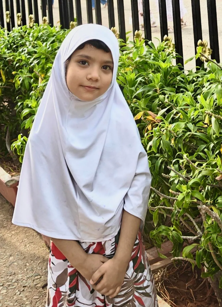 A young learner in a white hijab standing in a garden
