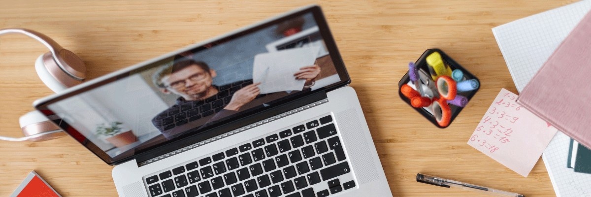 A laptop on a desk showing a teacher in a live class